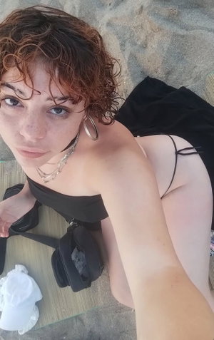 Woman with curly hair in black top lying on textured surface, holding camera for selfie.