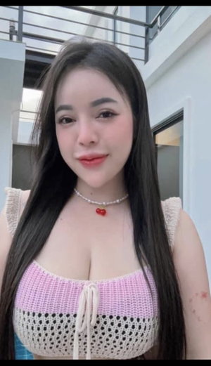 Buxom Asian woman in pink crochet top, necklace, indoors.