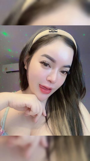 Woman with long dark hair wearing headband and lace top indoors.