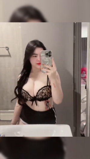 Woman with long dark hair in lace bra taking bathroom mirror selfie.