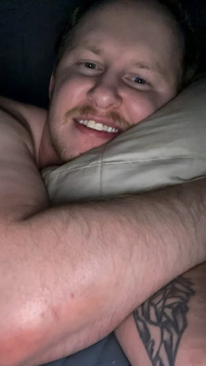 Shirtless bearded man lying in bed.