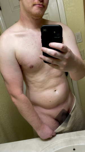 Shirtless man in towel takes bathroom mirror selfie.
