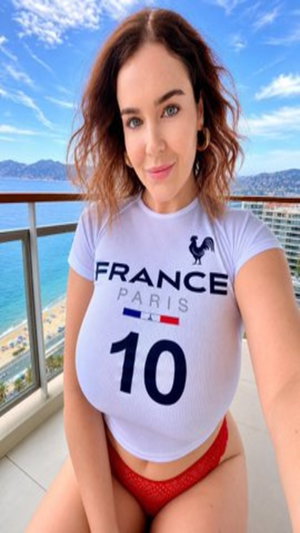 Woman in white France shirt and red underwear posing on balcony with ocean view.