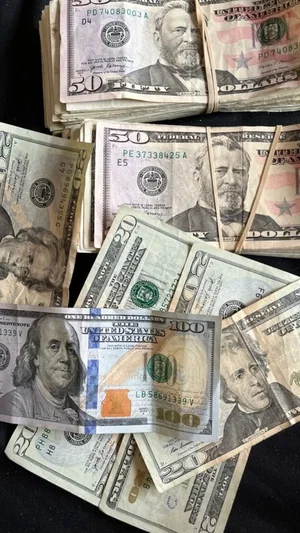 Stacks of US dollar bills including $50 and $100 denominations on a dark surface.