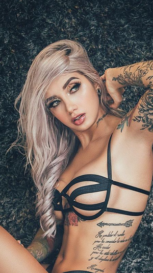 Blonde woman in black strappy lingerie on dark surface.