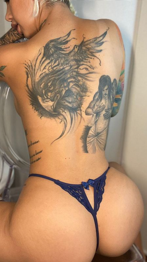 Woman with tattoos on back wearing blue lace thong, sitting indoors.