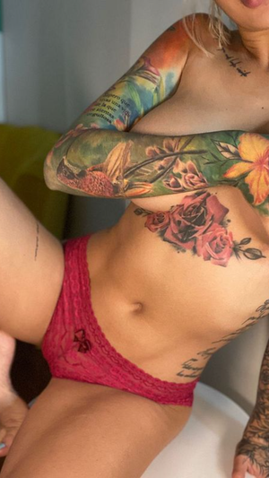 Tattooed blonde woman in pink lingerie posing indoors.