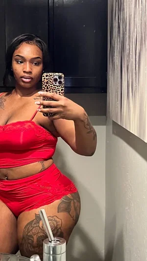 Woman in red lingerie with tattoos takes mirror selfie in indoor setting.