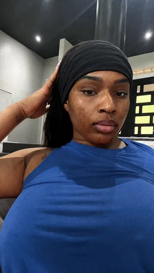 Woman with dark skin wearing blue top and black headband, indoors, hand on head.