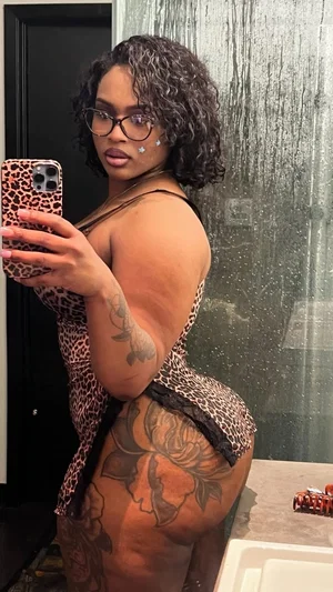 Woman with curly hair and tattoos wears leopard print lingerie in bathroom mirror selfie.