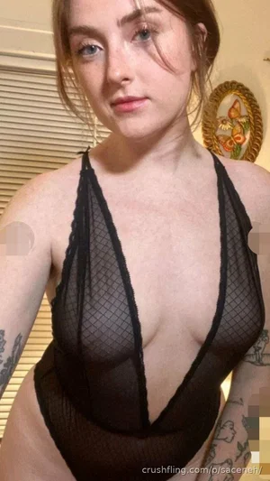 Woman in black mesh bodysuit with tattoos on arms, indoors.