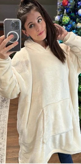 Woman in white hoodie taking selfie near Christmas tree.