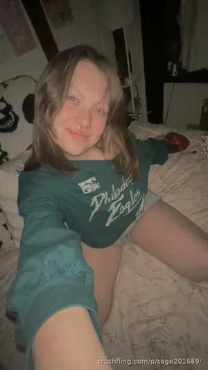 Woman in green Philadelphia Eagles shirt lying on bed, casual indoor selfie.