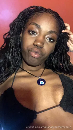Woman with braided hair wearing black fuzzy top and blue eye necklace, posing indoors.