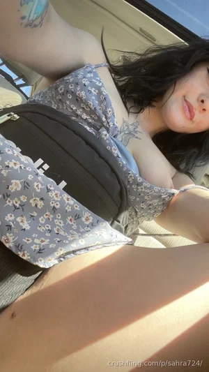 Woman with dark hair and tattoos in floral top, lying down indoors.