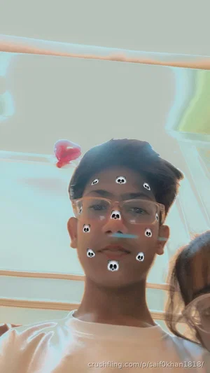 Young man with glasses and skull face filter, wearing white shirt, indoors.