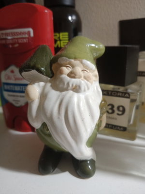 Ceramic gnome figurine with green hat on shelf with bottles.