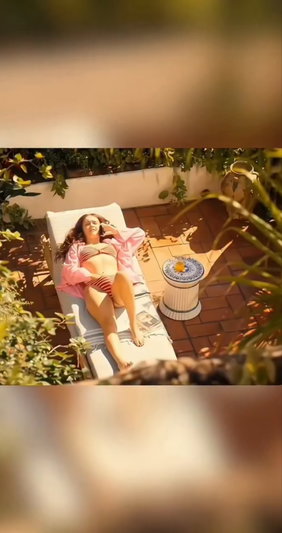 Woman in striped bikini and pink robe lying on lounge chair in garden.