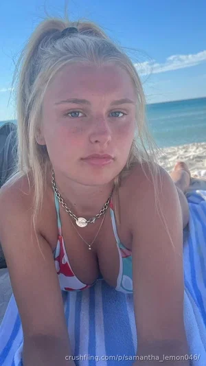 Blonde woman in colorful bikini top lying on blue striped towel at beach.