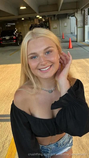 Blonde woman in off-shoulder black top and denim shorts, smiling in a parking garage.