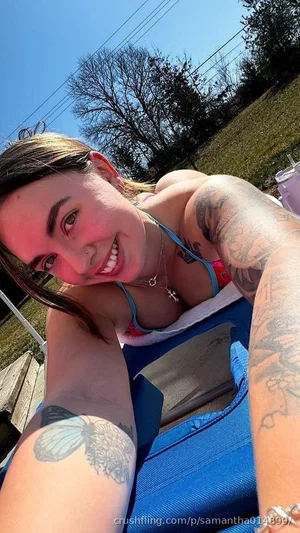 Woman with tattoos in bikini top, lying on blue blanket outdoors on sunny day.