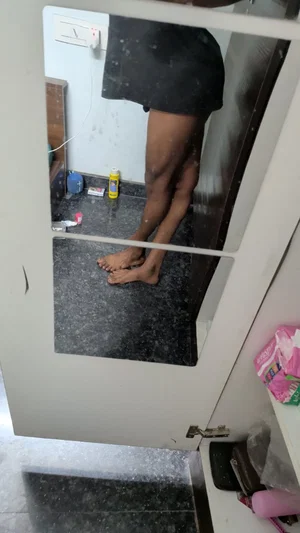 Person in black shorts standing barefoot in bathroom, viewed through mirror.