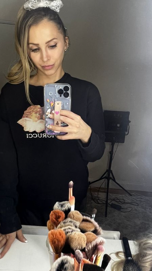 Woman with blonde hair in black long-sleeve shirt, holding phone for mirror selfie in indoor