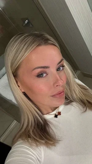 Blonde woman in white top, taking mirror selfie indoors.