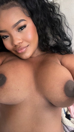 Woman with curly black hair and bare chest posing indoors.