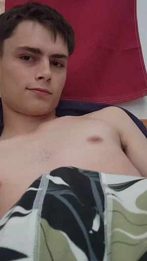Shirtless man with short dark hair lying down, wearing patterned shorts, indoors.