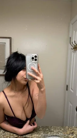 Woman with dark hair in maroon lingerie taking mirror selfie in bathroom.