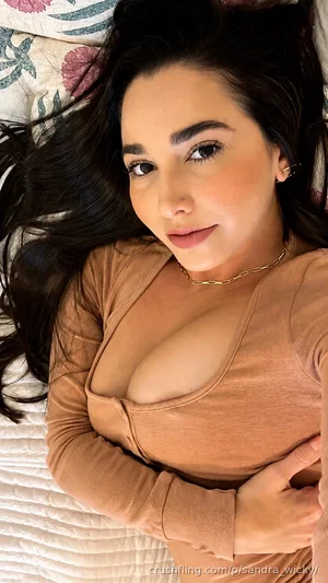 Woman with long dark hair in a brown top lying on a bed with floral pillows.