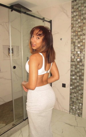 Woman in white top and gray skirt posing in bathroom with marble tiles.