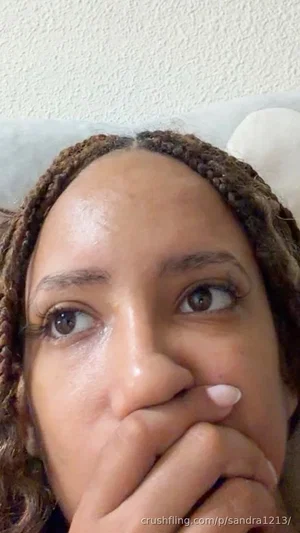 Woman with braided hair lying down, hand near mouth, indoor setting.