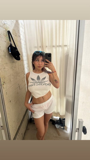 Woman in white crop top and shorts taking mirror selfie indoors.