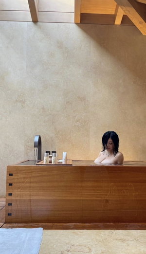 Asian woman with wet black hair in wooden bathtub.