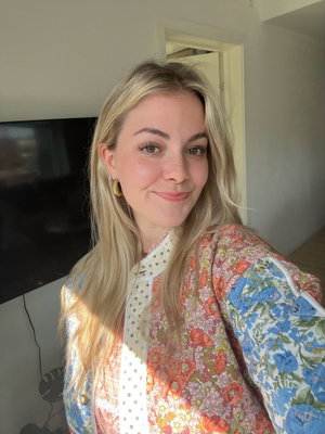 Blonde woman in floral jacket taking indoor selfie, smiling at camera.