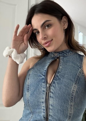 Woman with dark hair in denim top posing indoors.
