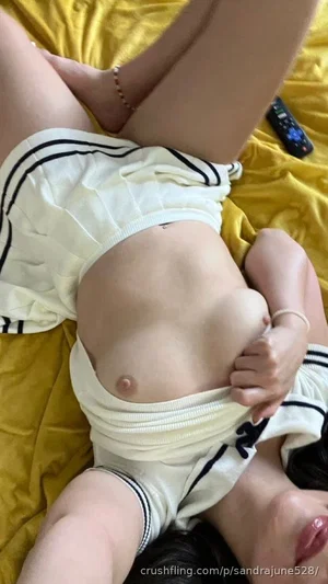 Woman in white shorts lying on yellow bed, pulling waistband down to expose lower abdomen.