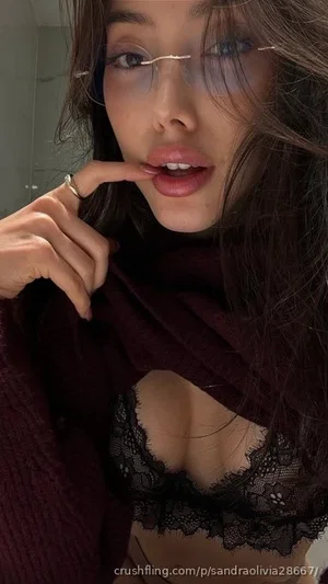 Woman with dark hair and glasses wears black lace bra under maroon sweater, indoors.