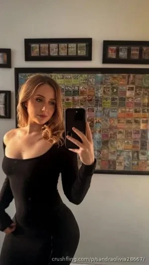 Woman in black off-shoulder dress taking mirror selfie in bedroom.