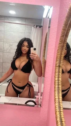 Woman in black bikini taking mirror selfie in pink bathroom.