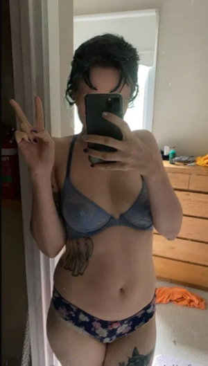 Woman in blue bra and patterned underwear taking mirror selfie in bedroom.