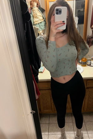 Brunette woman in floral crop top takes mirror selfie in bathroom.