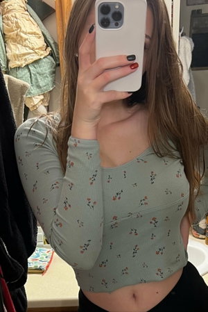 Woman in floral crop top and black bottoms taking mirror selfie in bathroom.
