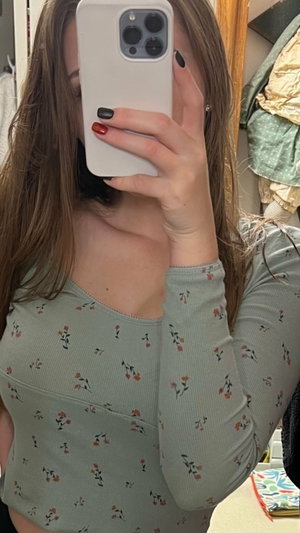 Woman in floral long-sleeve top taking mirror selfie, indoor setting.