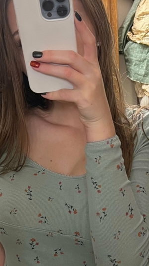 Woman with long brown hair in floral top taking mirror selfie indoors.
