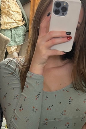 Woman in floral top taking mirror selfie, long hair, indoor setting.