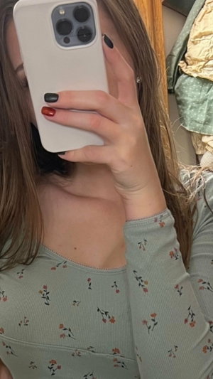 Woman with long hair in floral top taking mirror selfie indoors.