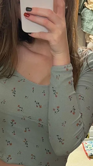 Woman in floral long-sleeve top taking mirror selfie, indoor setting.